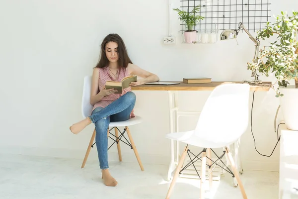 Lecture, éducation, culture, concept de personnes - une jeune étudiante lit un livre, alors qu'elle est assise sur une chaise dans une pièce blanche — Photo