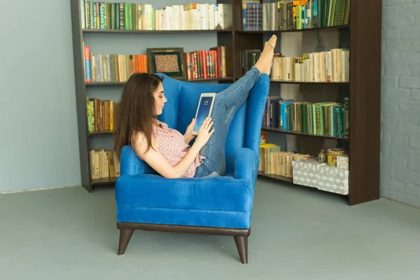 Lidé, vzdělávání a technologie koncept - žena čte digitální tabletu v křesle v knihovně — Stock fotografie