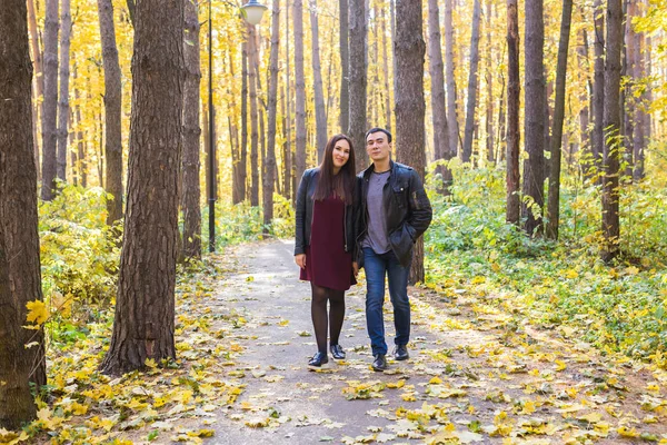 People, family and leisure concept - young couple walking in the autumn park