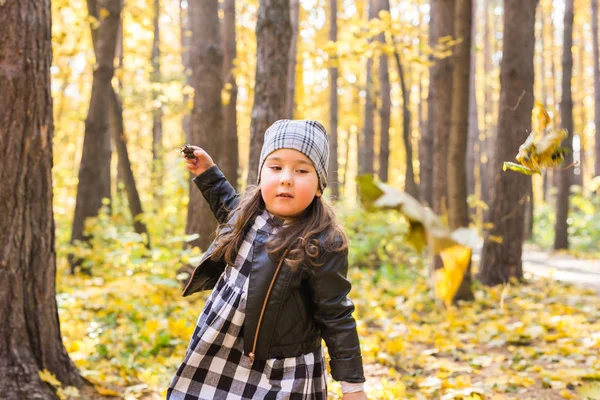 Concepto de niños, otoño y familia - niña jugando con hojas caídas en el parque —  Fotos de Stock