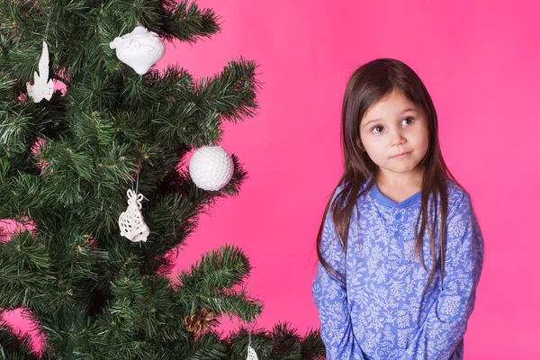 Παιδιά, αργίες και Χριστούγεννα έννοια - κοριτσάκι κοντά στο χριστουγεννιάτικο δέντρο σε ροζ φόντο — Φωτογραφία Αρχείου