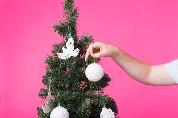 Dezember und Feiertage Konzept - man Hand schmücken Weihnachtsbaum auf rosa Hintergrund — Stockfoto