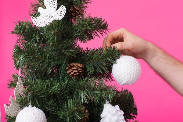 Koncepcja grudnia i wakacje - Mans ręka dekorowanie choinki na różowym tle — Zdjęcie stockowe
