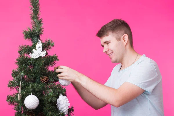 Emberek, a szünetek és a karácsonyi concept - a fiatalember díszítő karácsonyfa rózsaszín háttér — Stock Fotó