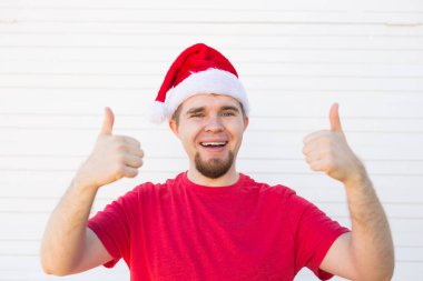 Beyaz arka plan üzerinde bir başparmak tabela yapım bir Noel şapka ile genç adam