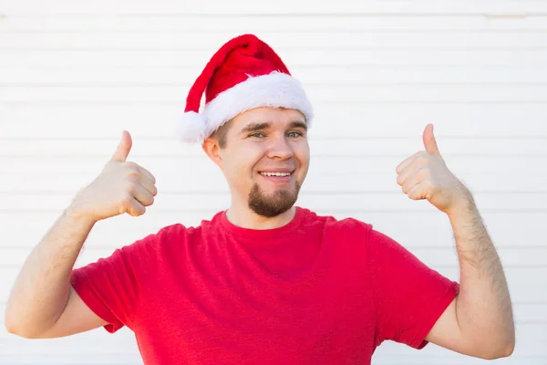 Jeune homme avec un chapeau de Noël faisant un signe pouce vers le haut sur fond blanc — Photo