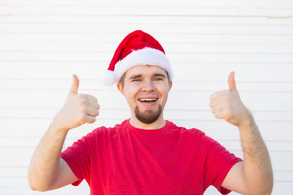 白い背景の上のサインを親指を作るクリスマスの帽子を持つ若者 — ストック写真