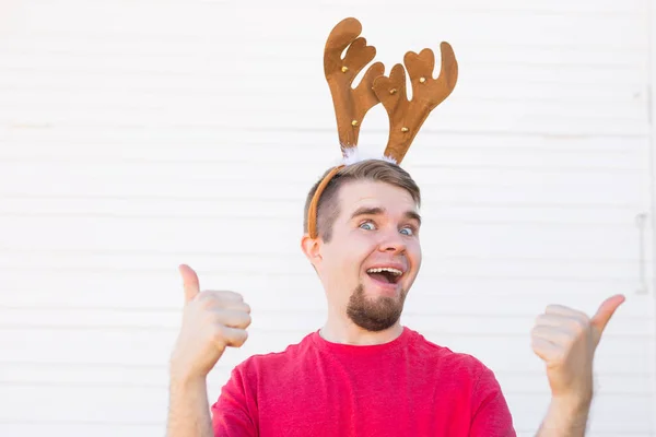 Concepto de vacaciones y Navidad - Joven con cuernos de ciervo con el pulgar hacia arriba gesto sobre fondo blanco — Foto de Stock