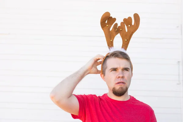 Christmas, holidays and people concept - a mans head with deer horns on it. Man scratches his head