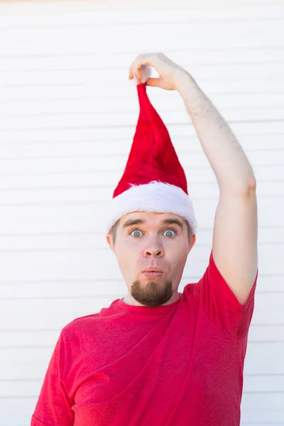 Urlaub, Weihnachten und Kleidungskonzept - überraschter lustiger gutaussehender Mann mit Weihnachtsmütze posiert auf weißem Hintergrund — Stockfoto