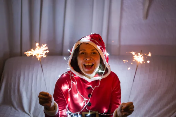 Noel ve tatil kavramı - maytap ışıklar holding Noel Baba şapkası olan mutlu kadın — Stok fotoğraf