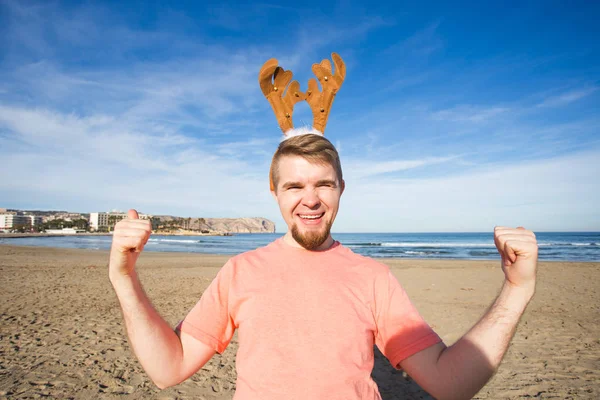 Gente, vacaciones y concepto de Navidad - joven disfrazado de venado santas en la playa —  Fotos de Stock