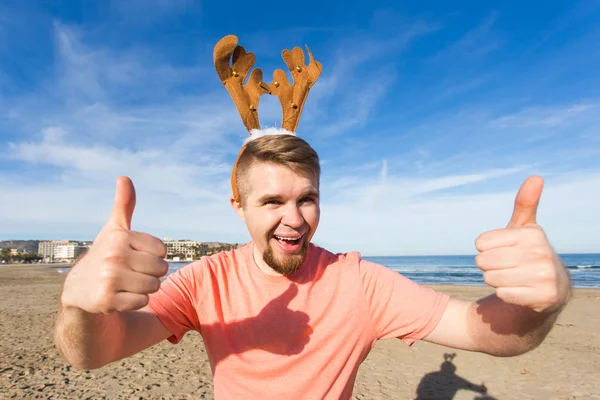 Feestdagen en Kerstmis concept - Man dragen rudolph hoorns met duimen omhoog op het strand — Stockfoto