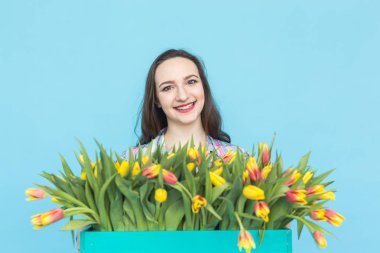 Gülüyor ve lale mavi arka plan üzerinde büyük kutu tutan mutlu beyaz kadın çiçekçi
