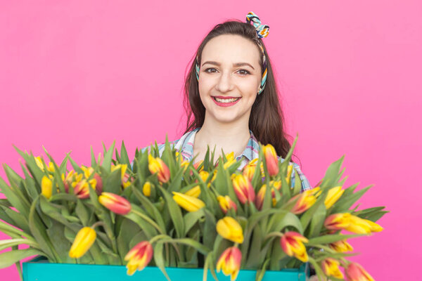 Close-up portrait of brunette young woman with bunch of tulips on pink background