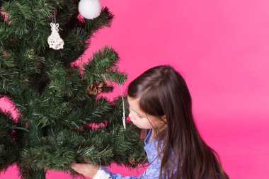 Çocuklar, tatil ve Noel kavramı - küçük kız pembe bir arka plan üzerinde Noel ağacı süsleme