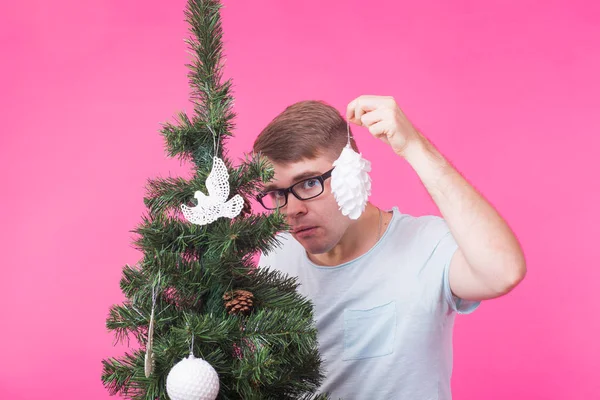 Navidad, vacaciones y el concepto de la gente - hombre feliz joven mostrar decoraciones de Navidad en el árbol de Navidad sobre el fondo rosa — Foto de Stock