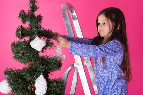 Kinder, Feiertage und Weihnachtskonzept - kleines Mädchen schmückt Weihnachtsbaum auf rosa Hintergrund — Stockfoto