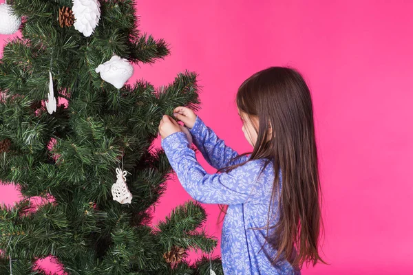 圣诞节和假日概念-一个小女孩在粉红色背景下装饰圣诞树 — 图库照片