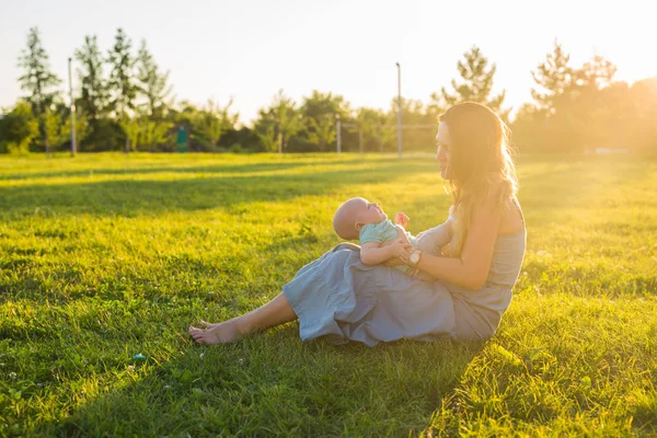 Ung kvinna med pojke på ängen på en solig dag. Lycklig familj på sommar solnedgång. Mor med baby. — Stockfoto