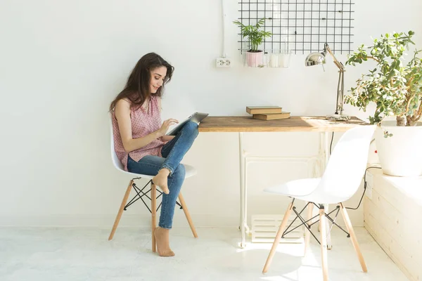 Technologies, communication, concept de personnes - la jeune femme est assise sur une chaise et bavarde sur une tablette numérique et sourit — Photo