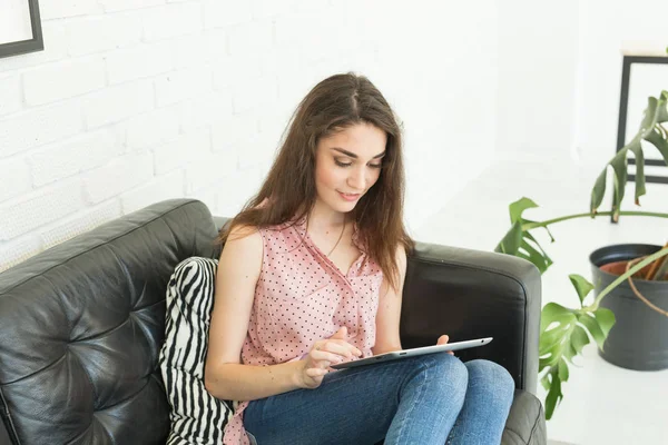Tecnologie, comunicazione, concetto di persone - giovane donna seduta sul divano in pelle e con tablet digitale — Foto Stock