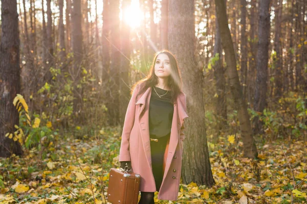 Otoño, naturaleza y concepto de personas - Retrato de una hermosa mujer sonriente con una maleta marrón caminando en otoño — Foto de Stock