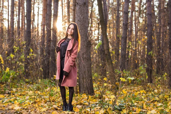 El tiempo, la estación, el concepto de la gente - mujer joven con abrigo rosa sobre el fondo de la naturaleza de otoño —  Fotos de Stock