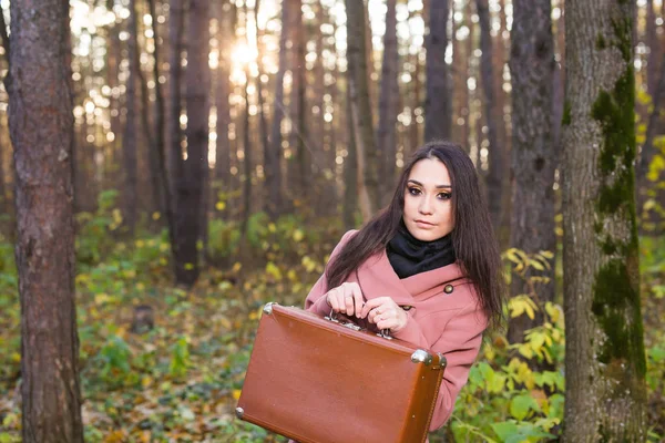 Moda, estação e conceito de pessoas - jovem feliz está indo em uma viagem com mala retro em um fundo de folhagem de outono — Fotografia de Stock