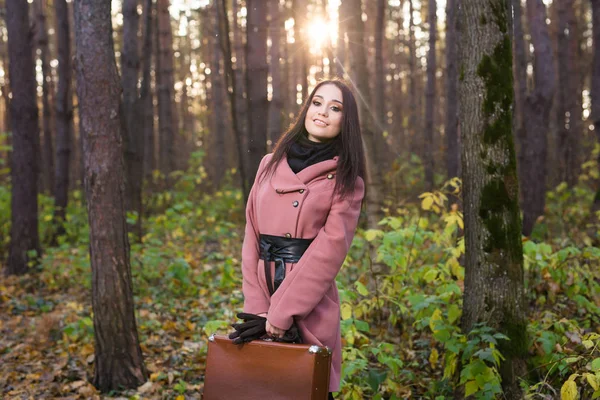 Женщина в осеннем парке гуляет с чемоданом — стоковое фото