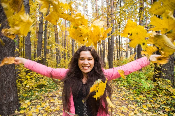 Autumn, joy and people concept - young woman having fun in autumn park. She is throwing yellow leaves in a sky