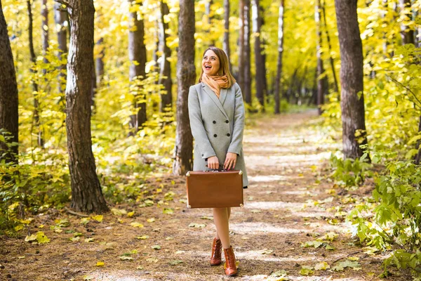 Outono, moda, conceito de pessoas - mulher com mala retro marrom andando pelo parque de outono e sorrindo — Fotografia de Stock