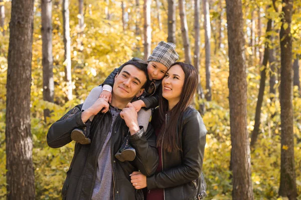 Lidé, rodina a volný čas koncept - šťastný otec drží malou dceru na zádech v podzimní park a matka — Stock fotografie