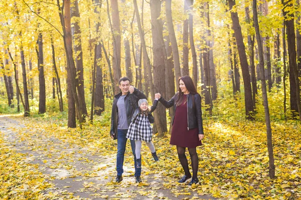 Mensen, familie en vrije tijd concept - gemengd ras vader en moeder hebben plezier in herfst park met hun dochter — Stockfoto