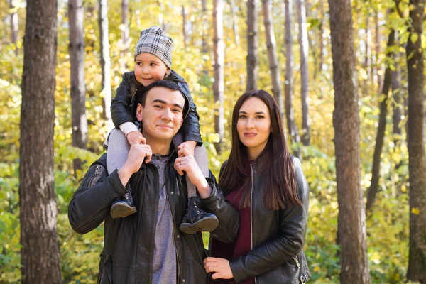 家族、秋、人々 コンセプト - 秋の公園で歩いている若い家族。お父さんの肩の上に座っている娘 — ストック写真