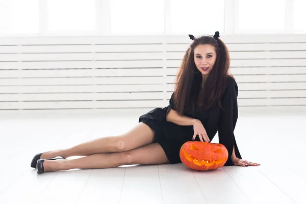 Femme brune souriante dans le maquillage d'Halloween posant avec citrouille sculptée — Photo