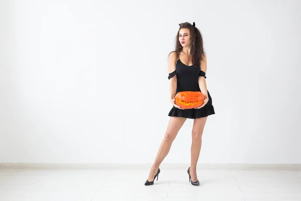 Portrait of a stylish brunette woman with halloween pumpkin over light background with copy space — Stock Photo, Image