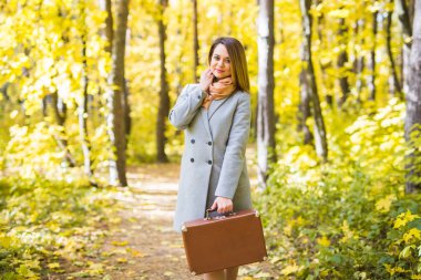 Moda, sezon ve insanlar kavramı - mutlu genç kadın retro çanta sonbahar yaprakları bir arka plan üzerinde bir yolculuğa çıkıyor