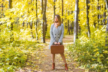 Moda, sezon ve insanlar kavramı - mutlu genç kadın retro çanta sonbahar yaprakları bir arka plan üzerinde bir yolculuğa çıkıyor