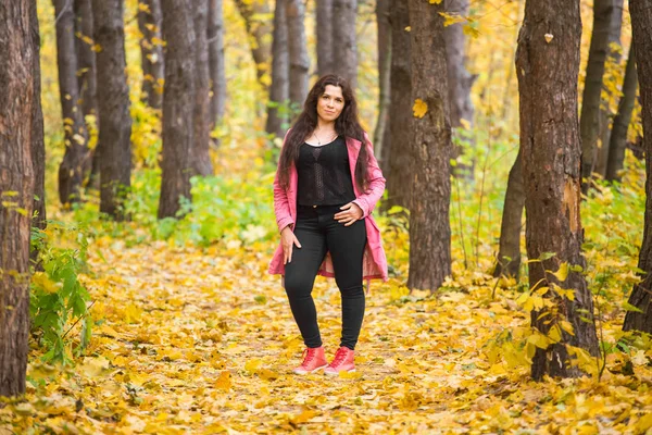 Concepto de temporada, moda y gente: mujer de talla grande en pantalones negros y chaqueta rosa de pie en el bosque de otoño — Foto de Stock