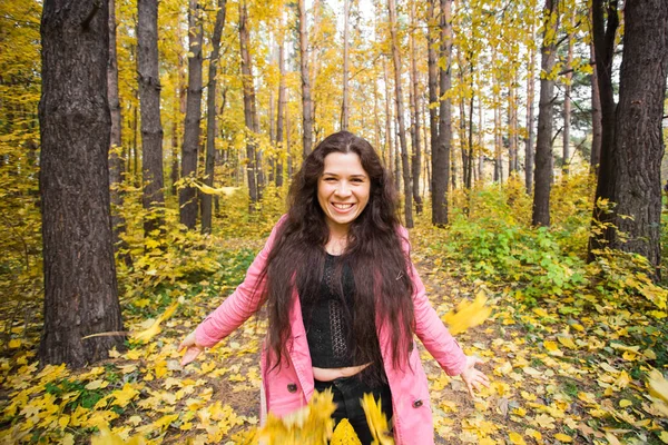 Autumn, happiness, people concept - young woman having fun in autumn park. She is throwing yellow leaves in a sky