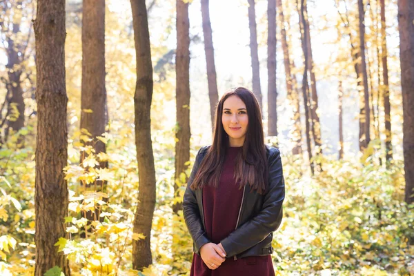 Autumn, nature, people concept - young beautiful woman walking in autumn park in red dress and black jacket
