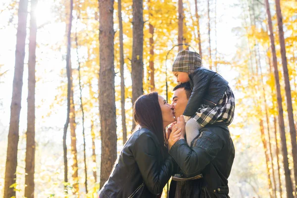 Familia, otoño, concepto de personas - familia joven caminando en el parque de otoño. Hija sentada sobre los hombros de los papás —  Fotos de Stock