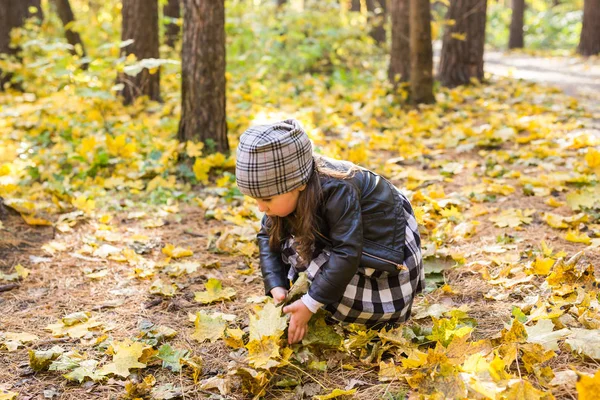 Concepto de niños, otoño y familia - niña jugando con hojas caídas en el parque —  Fotos de Stock