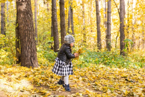 Φθινόπωρο, εποχές και τα παιδιά της έννοιας - ευτυχισμένη κοριτσάκι γελώντας και παίζοντας με πεσμένα φύλλα στο πάρκο — Φωτογραφία Αρχείου