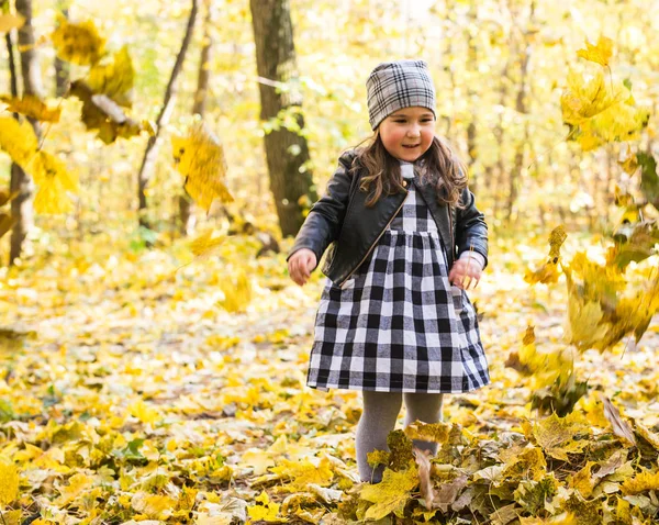 Concepto de niños, otoño y familia - niña jugando con hojas caídas en el parque —  Fotos de Stock