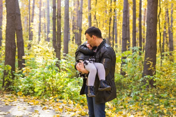 Paternidad, familia y concepto de ocio - padre sosteniendo a su pequeña hija en sus brazos en el parque de otoño — Foto de Stock