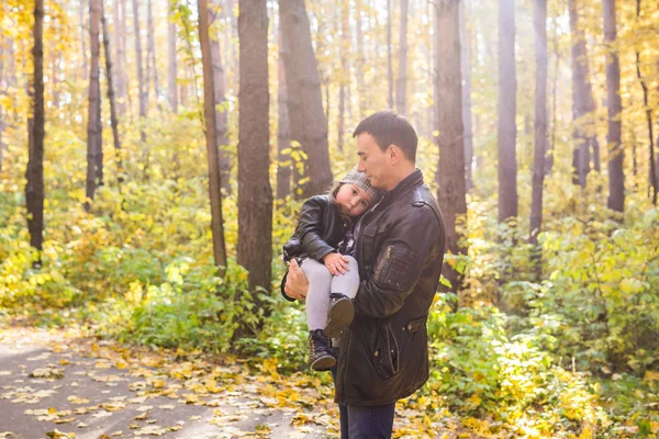 Paternidad, familia y concepto de ocio - padre sosteniendo a su pequeña hija en sus brazos en el parque de otoño — Foto de Stock