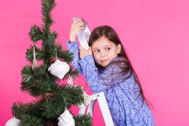 Çocuklar, tatil ve Noel kavramı - pembe bir arka plan üzerinde Noel ağacı yakınındaki küçük kız