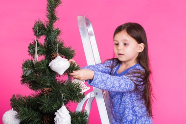 Çocuklar, tatil ve Noel kavramı - küçük kız pembe bir arka plan üzerinde Noel ağacı süsleme